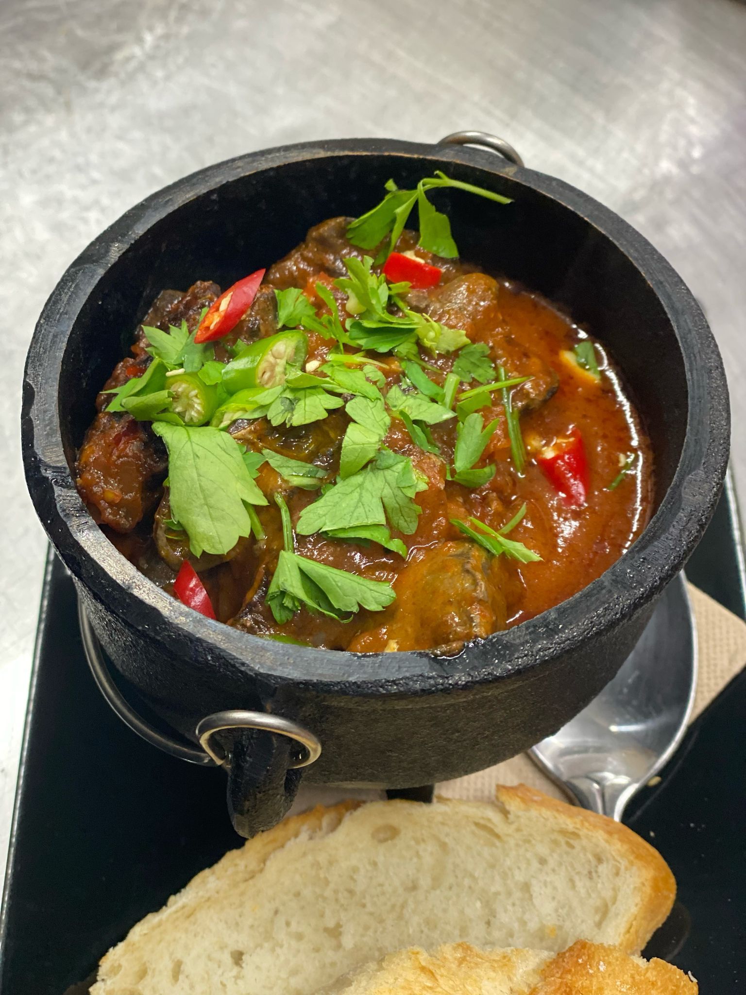 A bowl of stew with a piece of bread next to it.