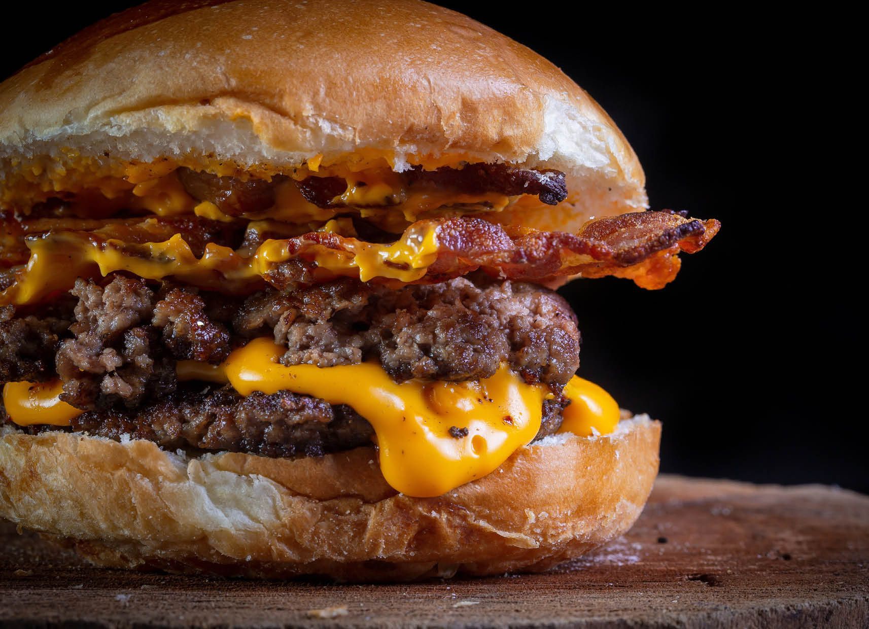 A close up of a hamburger with cheese and bacon on a wooden cutting board.