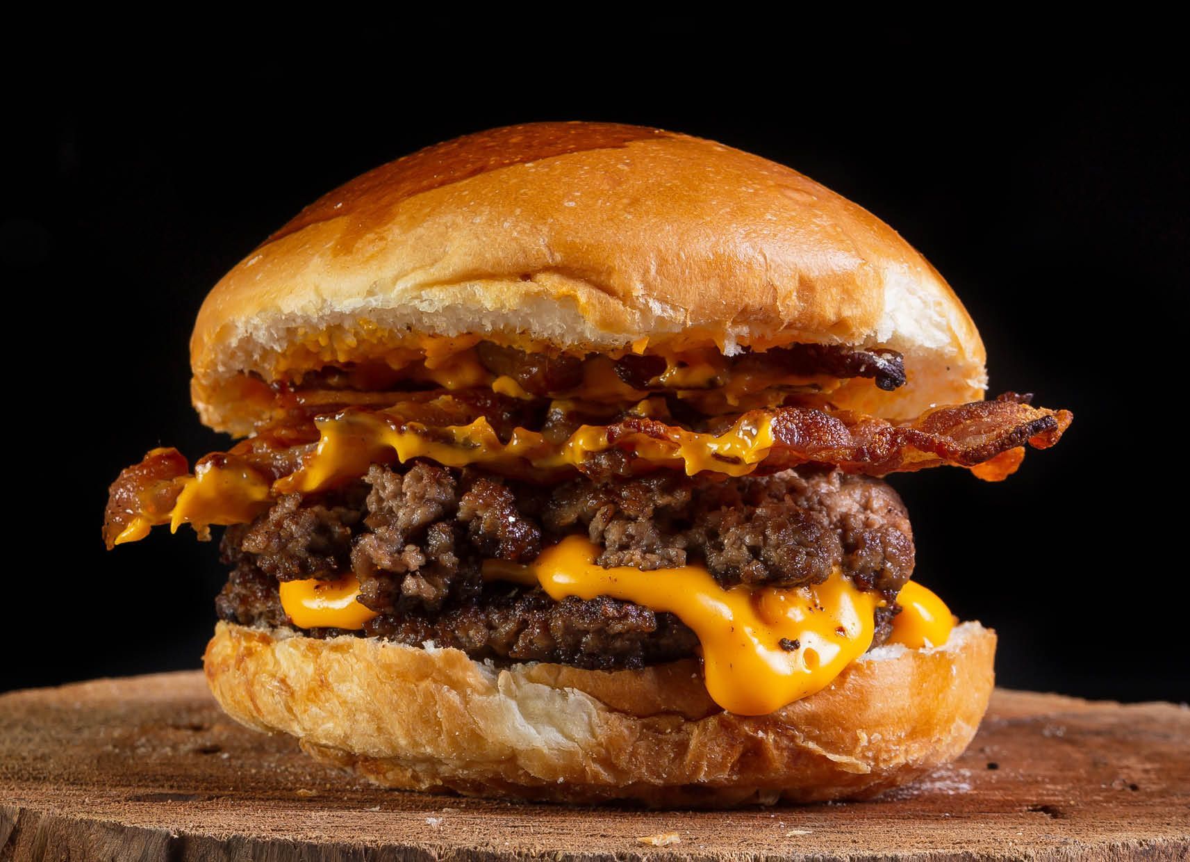 A close up of a hamburger with cheese and bacon on a wooden cutting board.