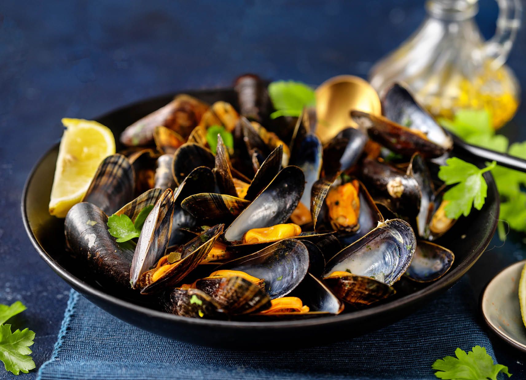 A bowl of mussels with lemon and parsley on a table.
