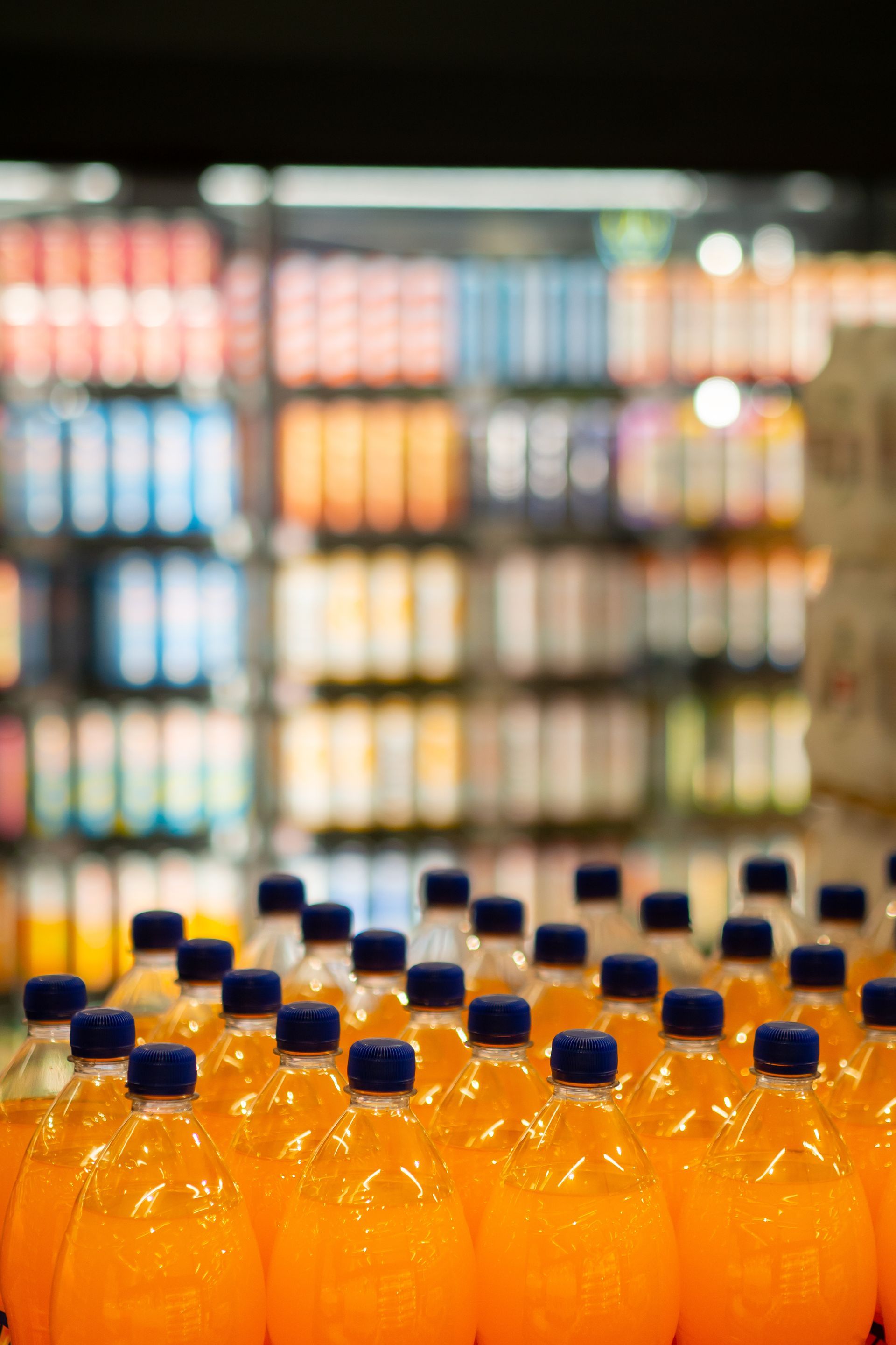 Bouteilles de soda à l'orange dans un réfrigérateur de supermarché, arrière-plan flou de diverses boissons.