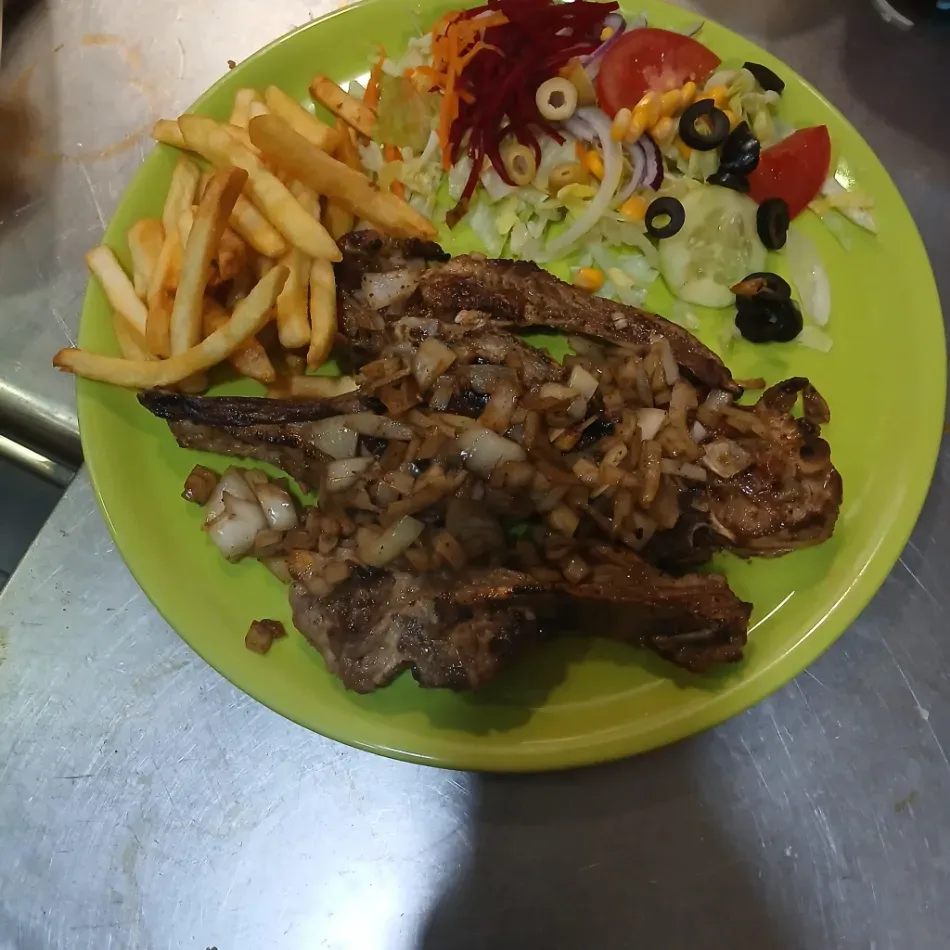 Grilled steak with onions, fries, and salad on a green plate