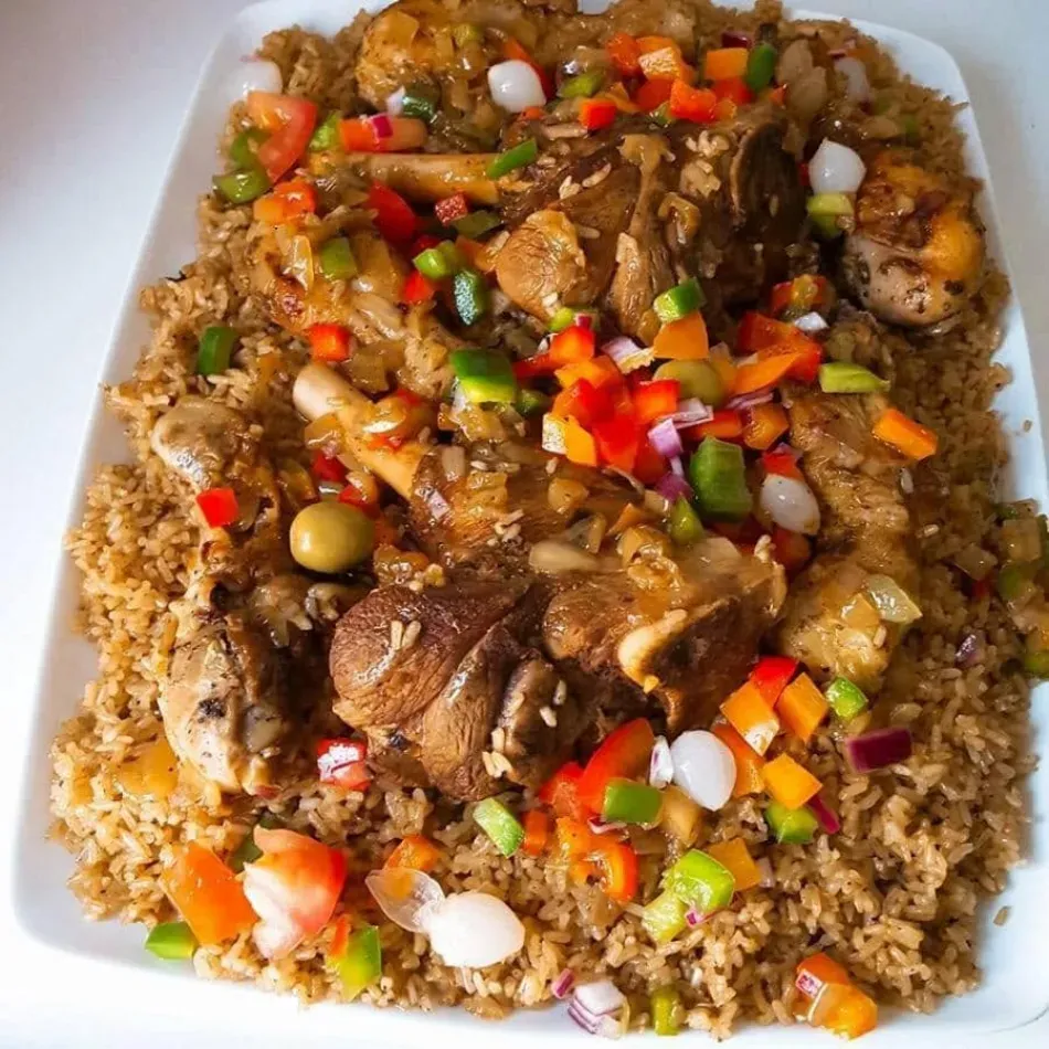 Plato de arroz cubierto con carne y coloridas verduras cortadas en dados en un plato blanco.