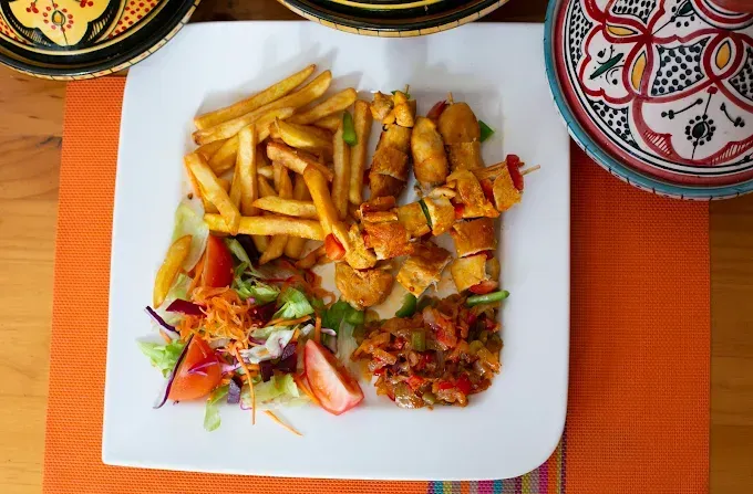 Plato de patatas fritas, brochetas a la parrilla y ensalada sobre un mantel individual naranja en una mesa.