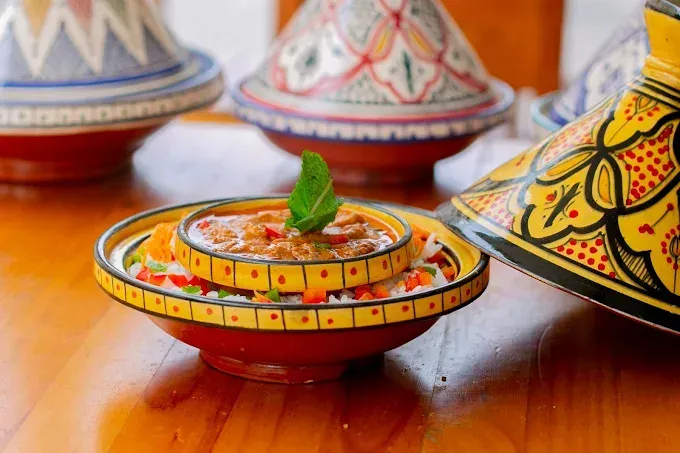 Bol de arcilla pintado de colores con postre sobre una mesa de madera, con macetas decorativas al fondo.
