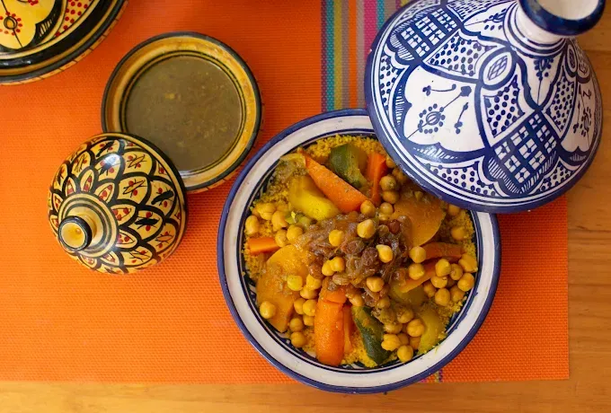 Comida al estilo marroquí servida en cuencos azules y blancos sobre un mantel naranja, con una tetera y una taza decorativas.