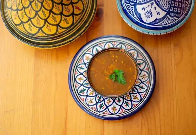 Tres cuencos decorados sobre una mesa de madera, uno de ellos con sopa y hierbas.