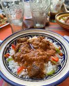 طبق أرز مغطى باللحم المفروم والخضراوات على طبق ذي حافة زرقاء، مع وجود أكواب في الخلفية