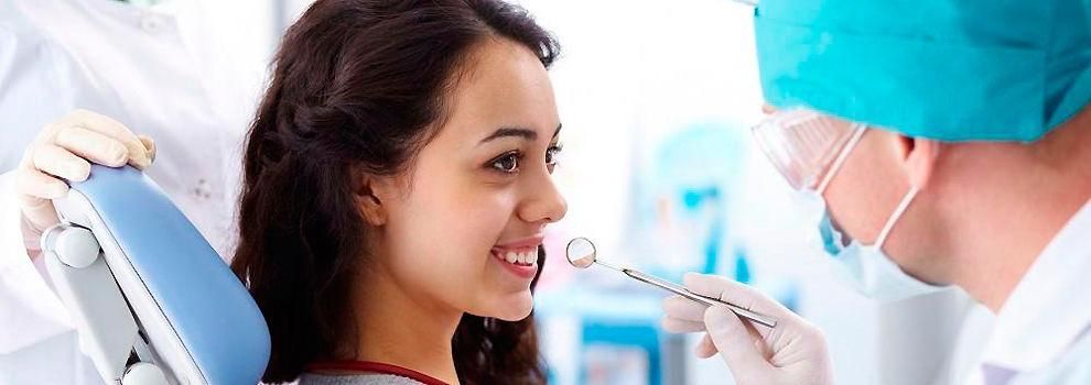 Una mujer está sentada en una silla dental mientras un dentista le examina los dientes.
