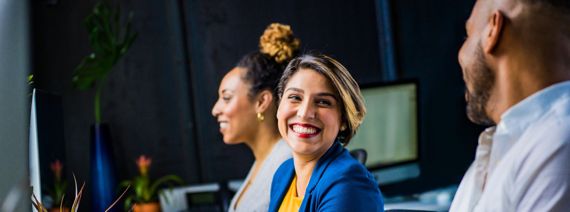 Un grupo de personas están sentadas en una mesa frente a una computadora y sonriendo.