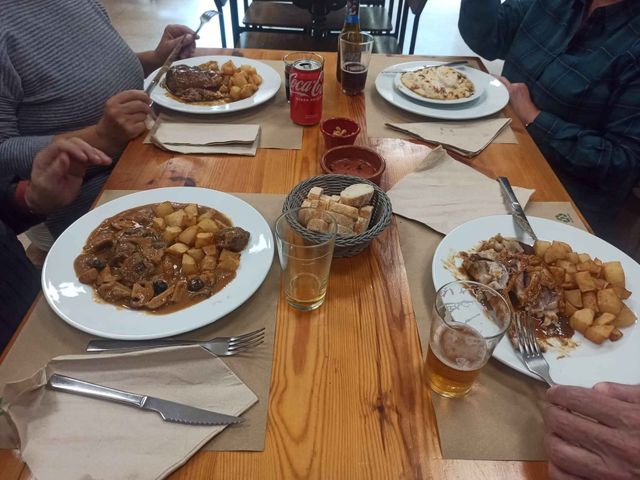 Un grupo de personas está sentado en una mesa con platos de comida y bebidas.