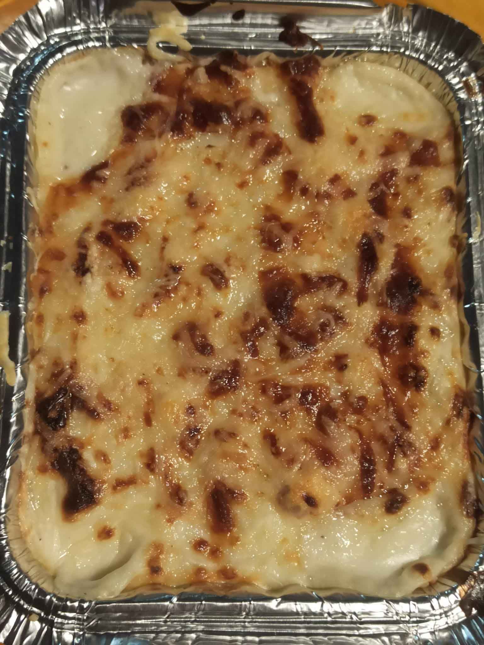 Un primer plano de una lasaña en un recipiente de papel de aluminio.