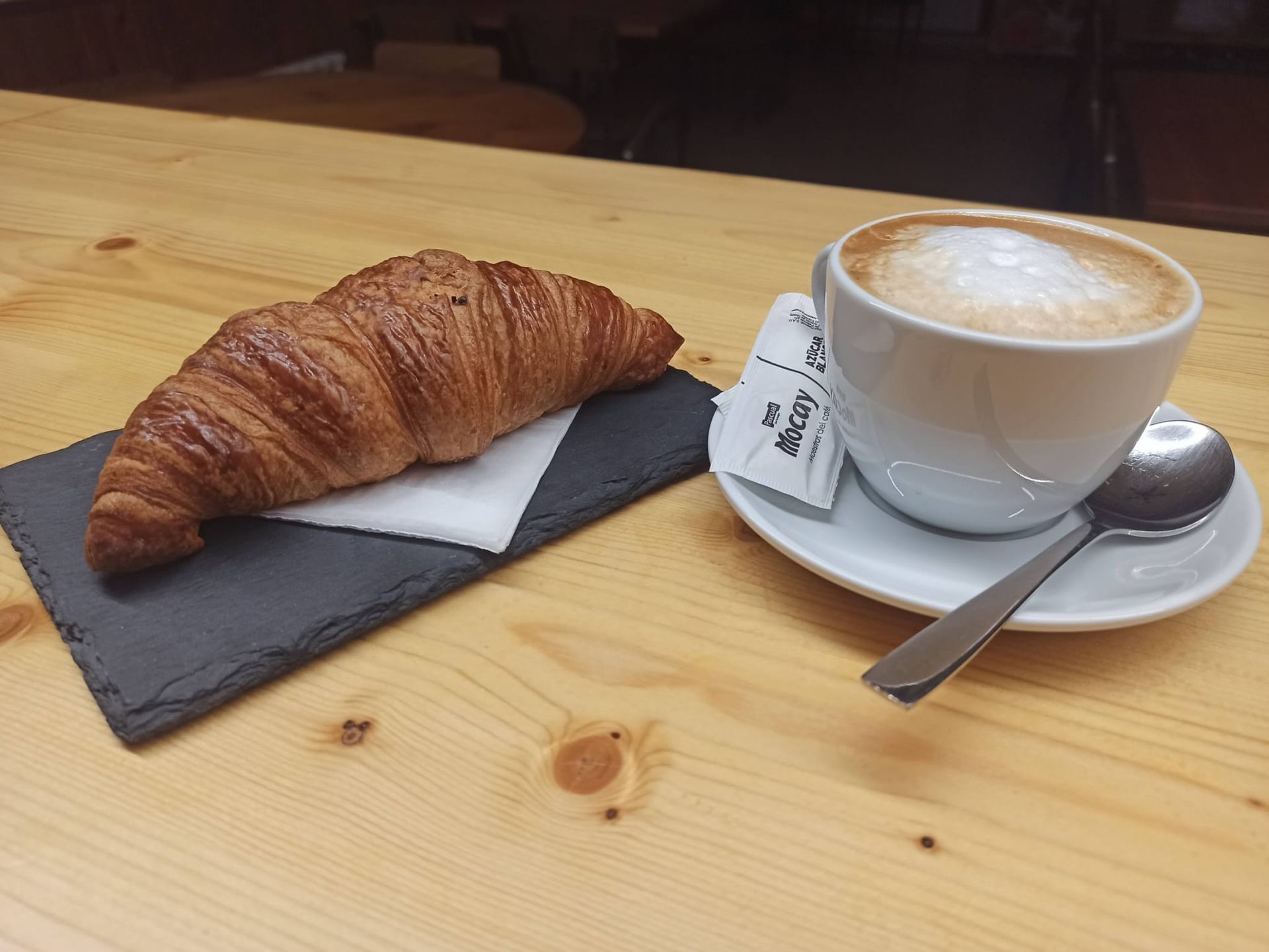Un croissant y una taza de café están sobre una mesa de madera.