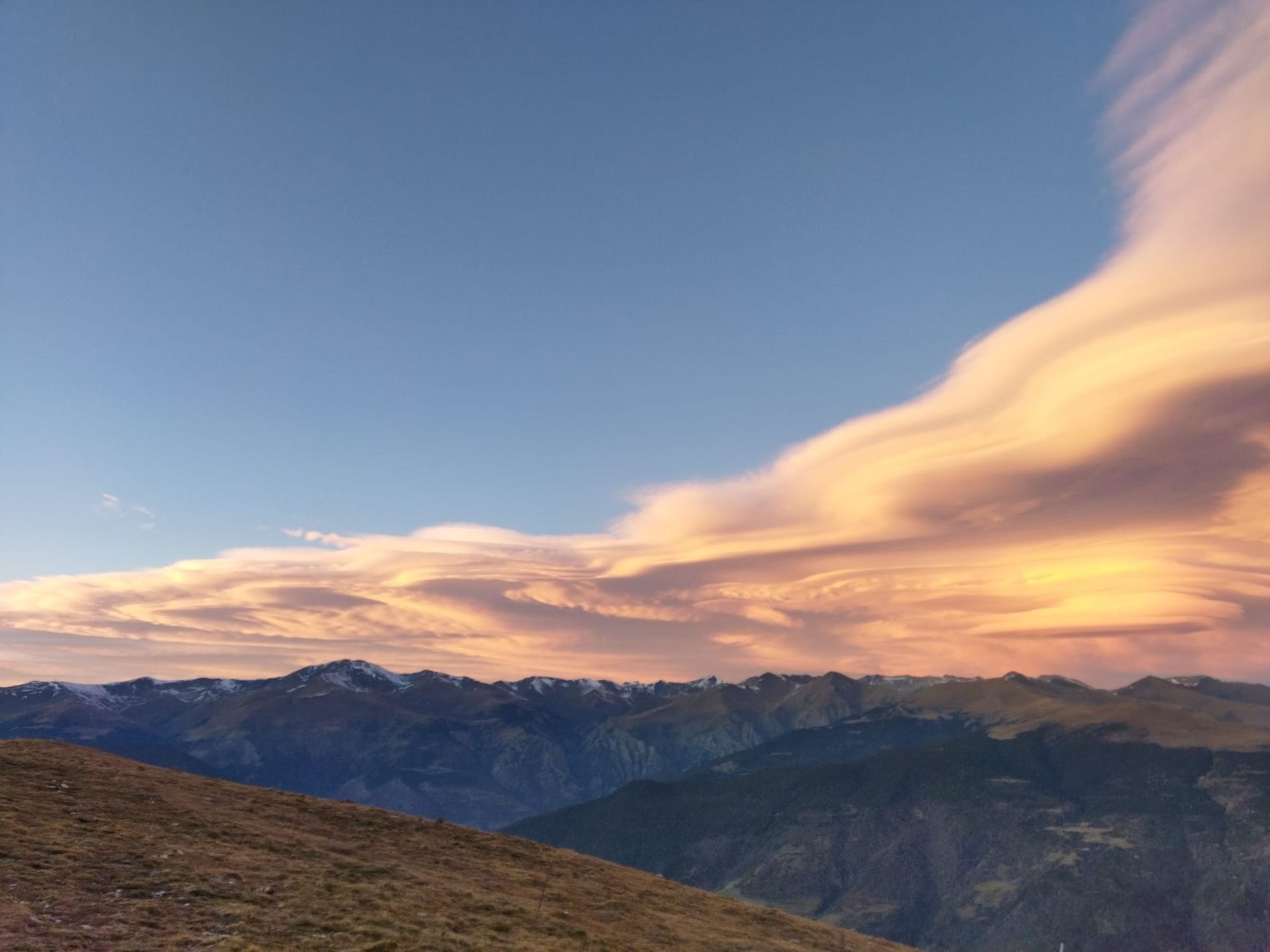 Una puesta de sol sobre una cadena montañosa con nubes en el cielo.