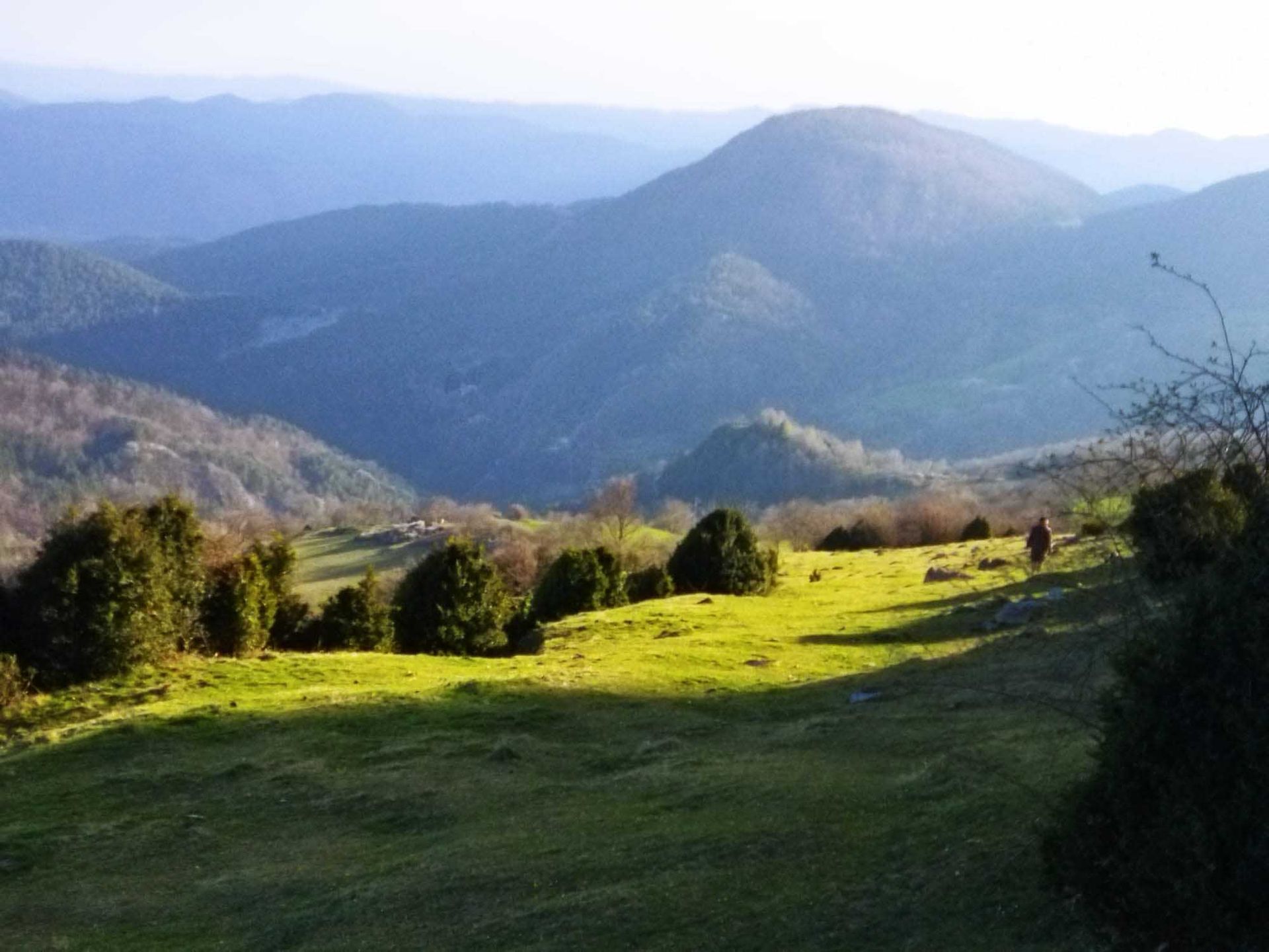 Una persona camina por un campo con montañas al fondo.