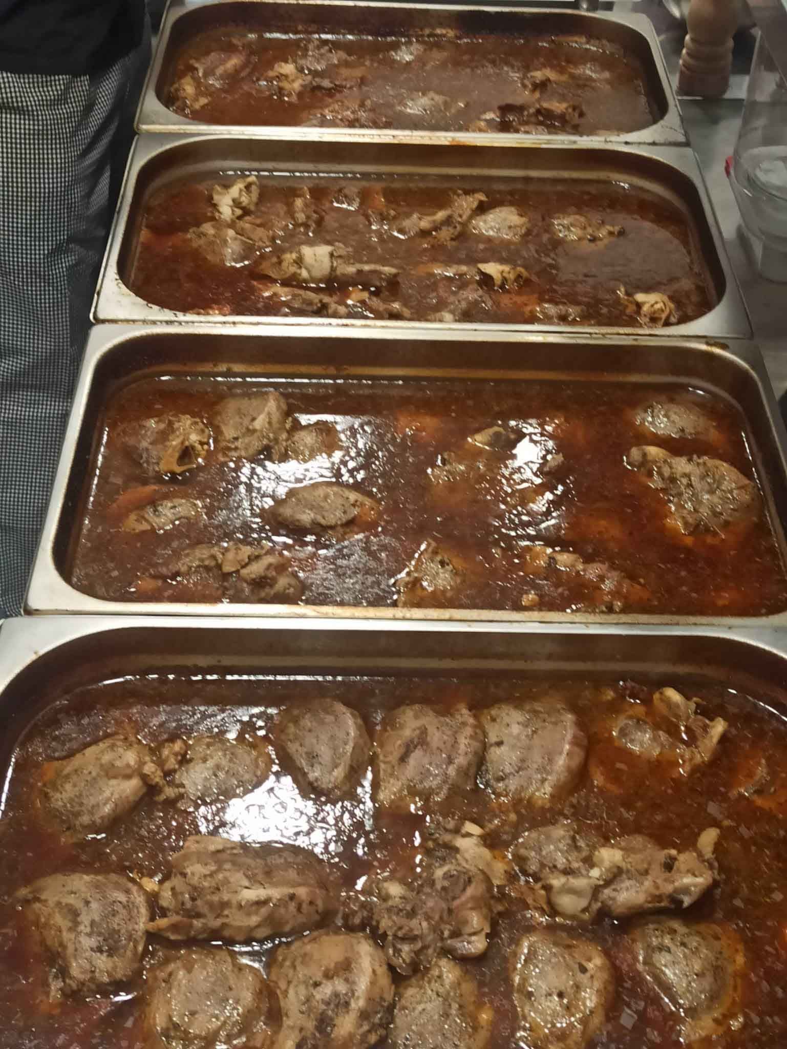 Una fila de sartenes llenas de carne y salsa sobre una mesa.