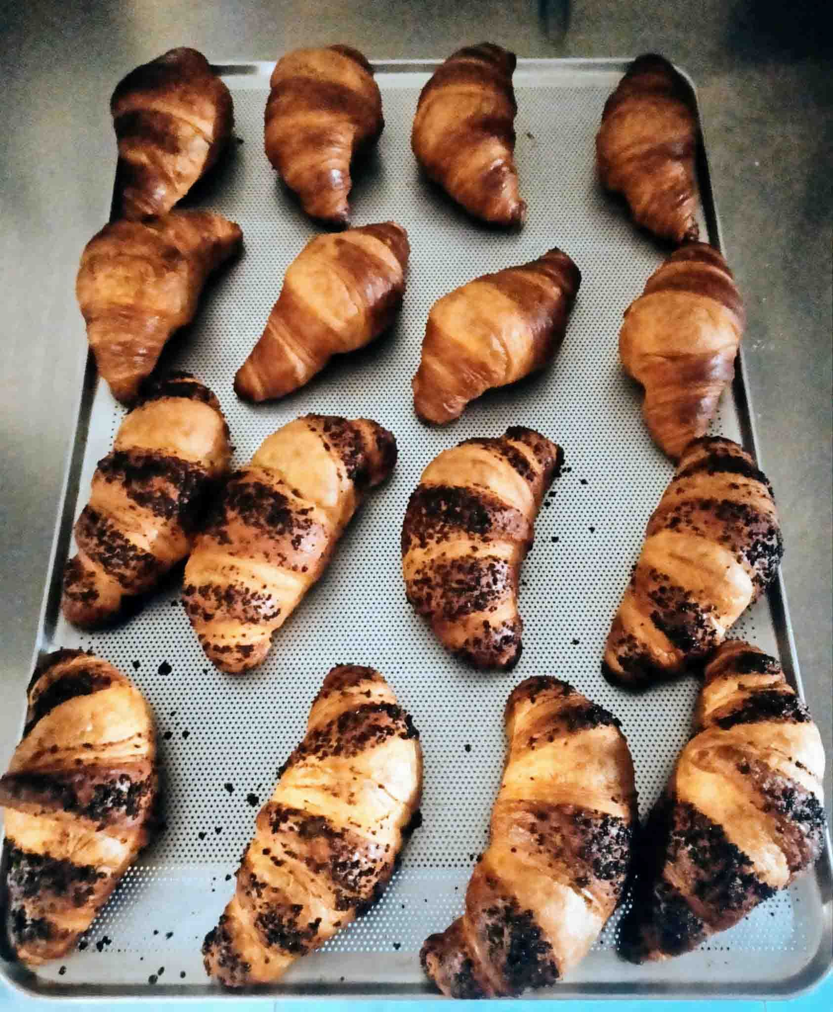 Un montón de croissants están sobre una bandeja de metal.
