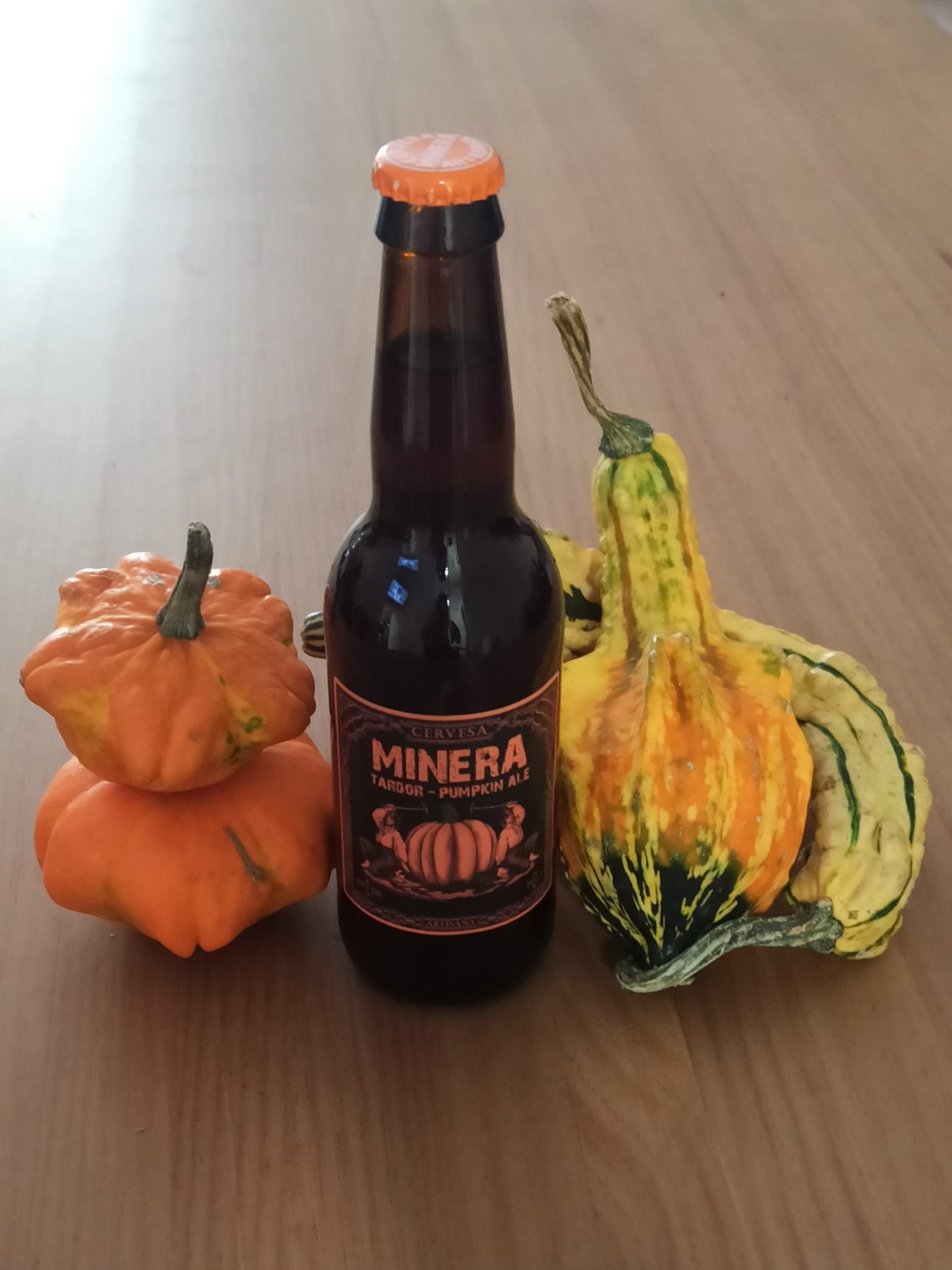Una botella de cerveza Minera está sobre una mesa junto a calabazas.