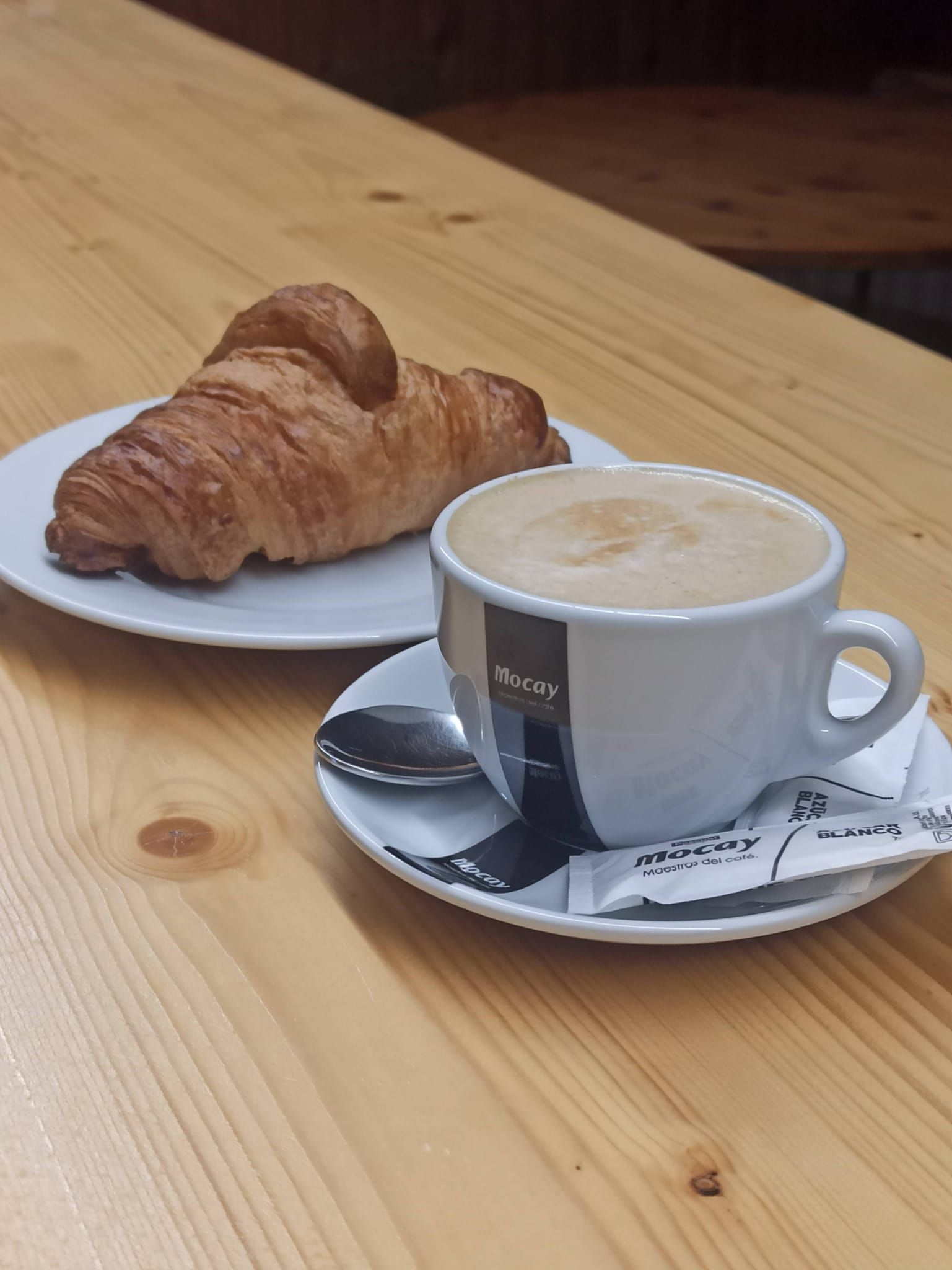Una taza de café y un croissant en una mesa de madera.