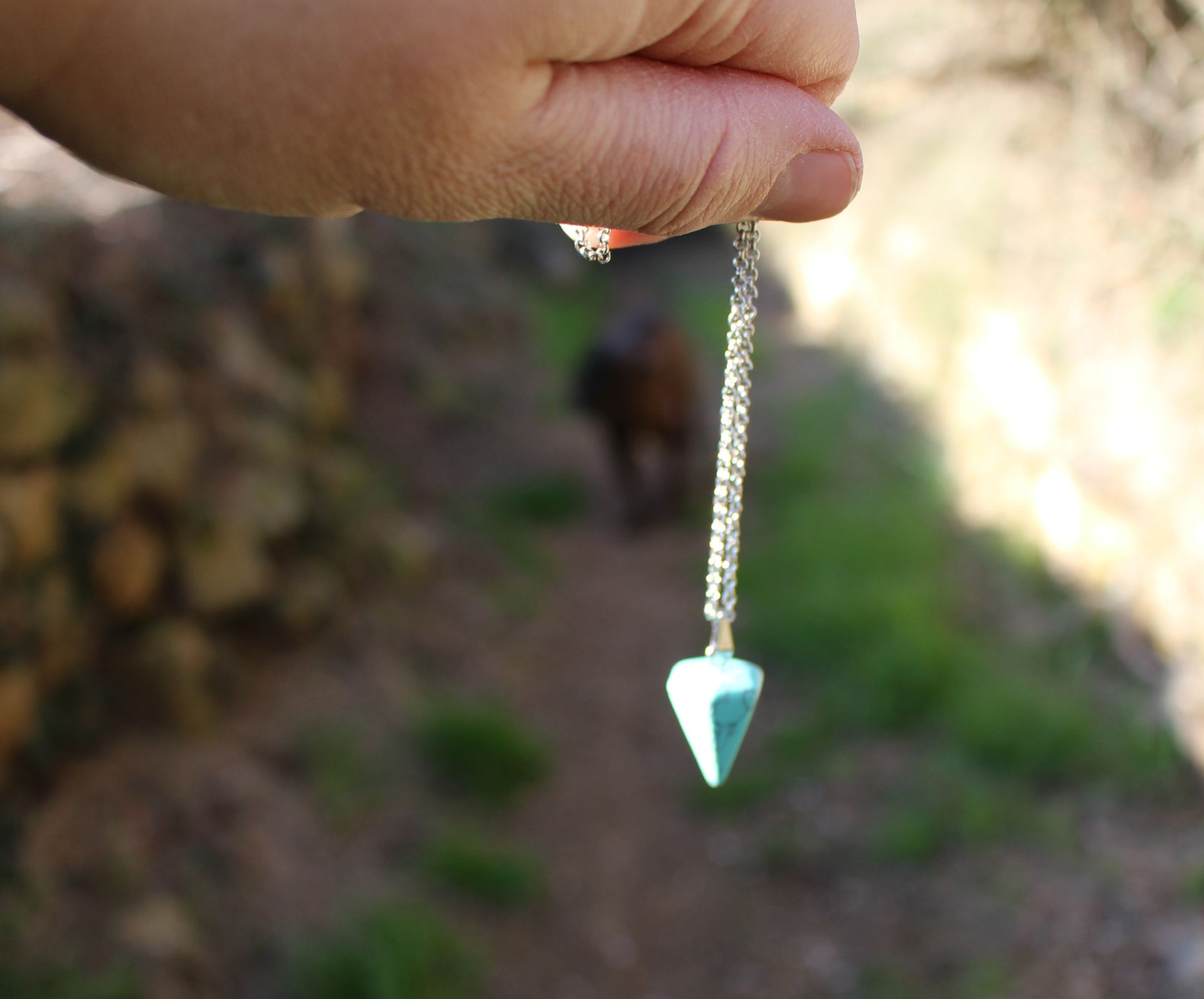 Une main tenant un pendule en extérieur.