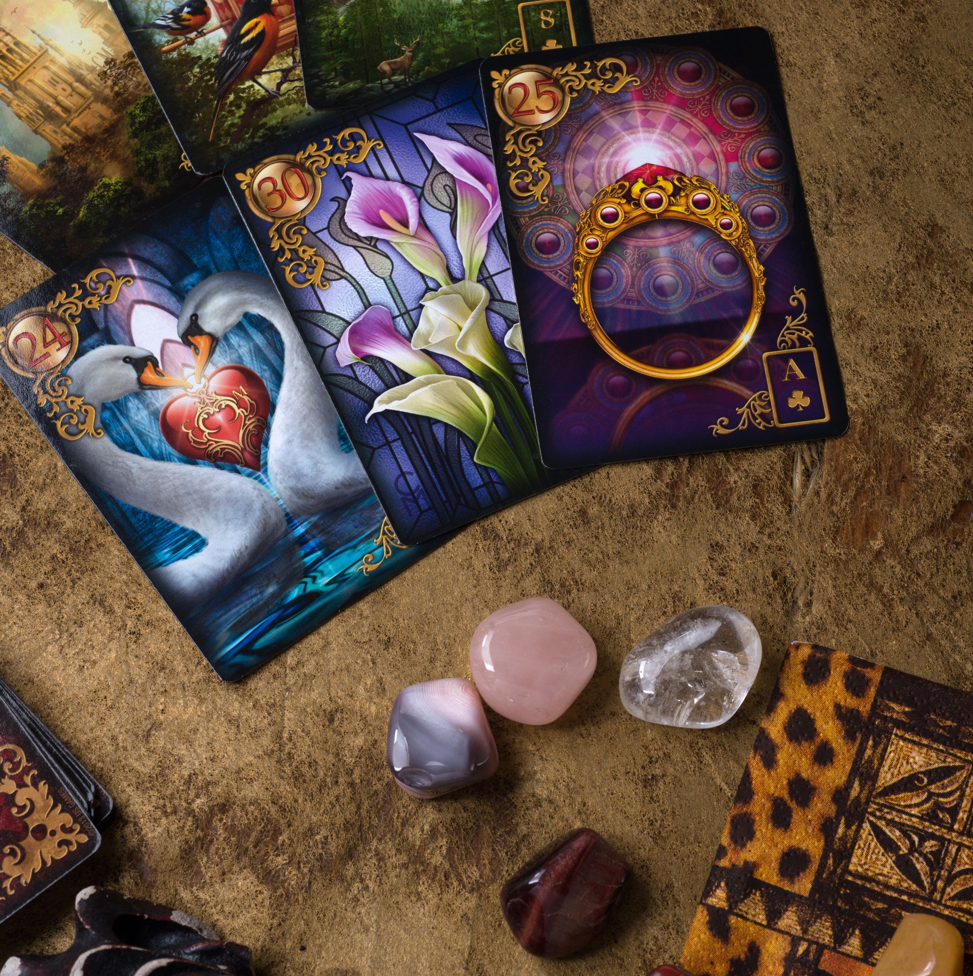 Cartes de tarot et cristaux sur un fond doré ; les cartes représentent des cygnes, des fleurs et une bague.