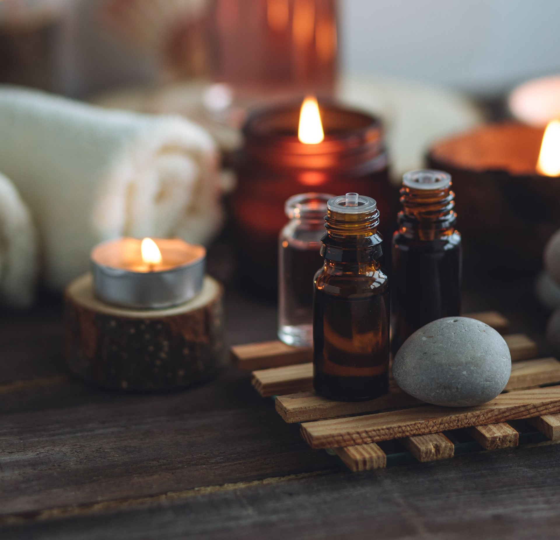 Scène de spa : bougies, flacons d’huiles essentielles, serviette roulée, éléments en bois et pierre. Tons chauds et accueillants.