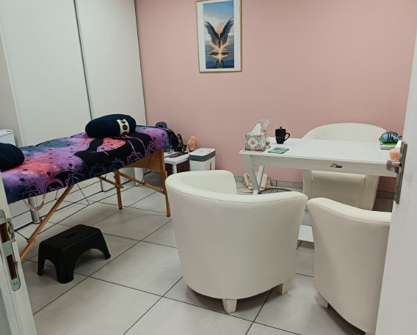 Une salle de massage avec une table de soins, des chaises et un bureau ; des murs rose pâle.