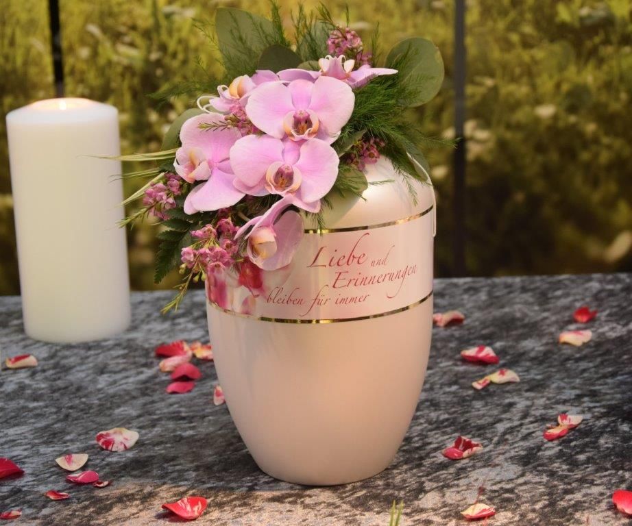 Eine Vase mit rosa Blumen steht neben einer Kerze auf einem Tisch.
