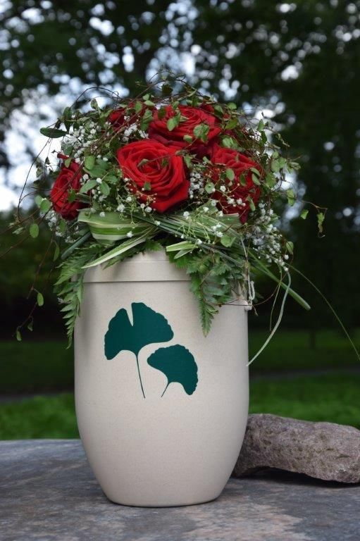 Eine weiße Vase gefüllt mit roten Rosen und grünen Blättern.