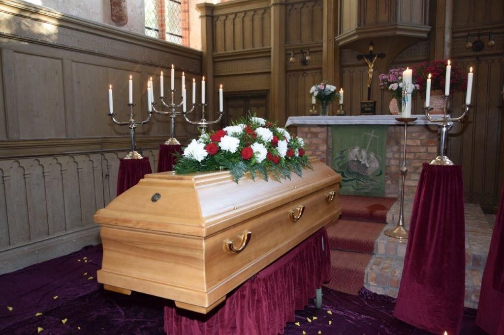 Ein Sarg steht mit Kerzen auf einem Tisch in einer Kirche.