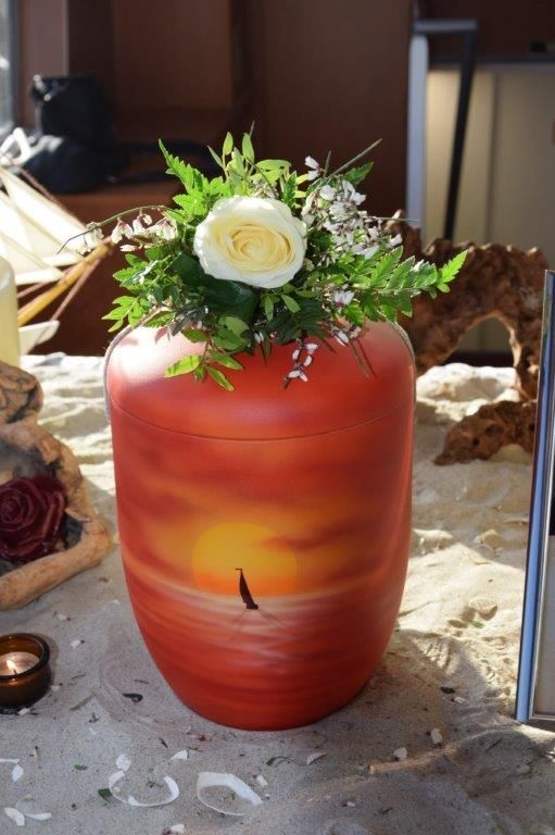 Eine rote Vase mit Blumen darin steht auf einem Tisch