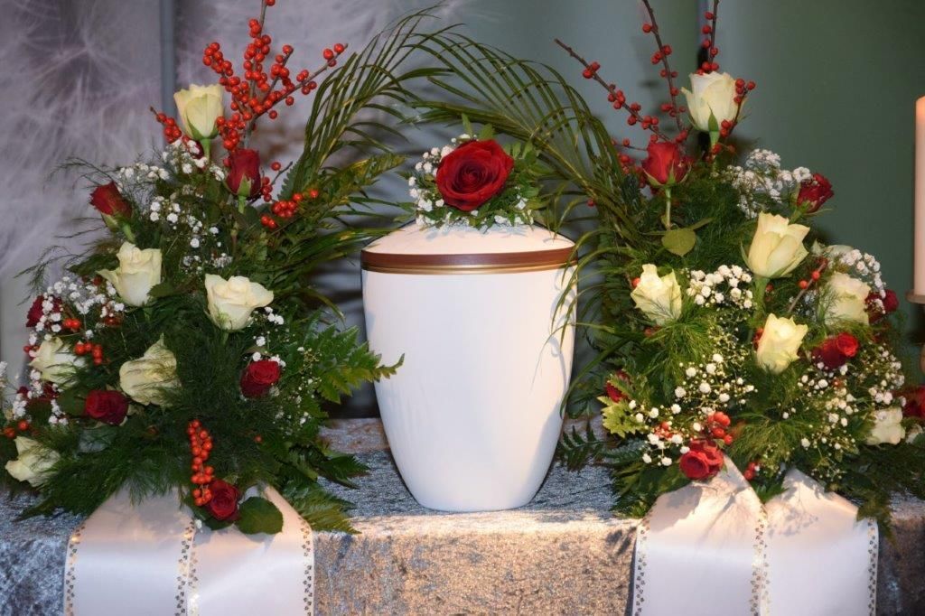 Eine weiße Urne ist von Blumen umgeben auf einem Tisch.