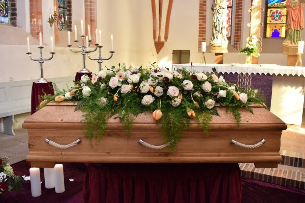 Ein Holzsarg mit Blumen und Kerzen in einer Kirche.