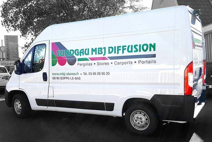 Fourgon de livraison blanc avec le logo « Strong (M) Diffusion », garé à l’extérieur près d’arbres et de bâtiments