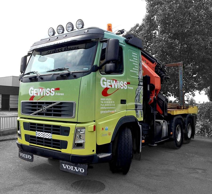 Camion-grue Volvo vert et orange avec le logo GEWISS, stationné à l’extérieur