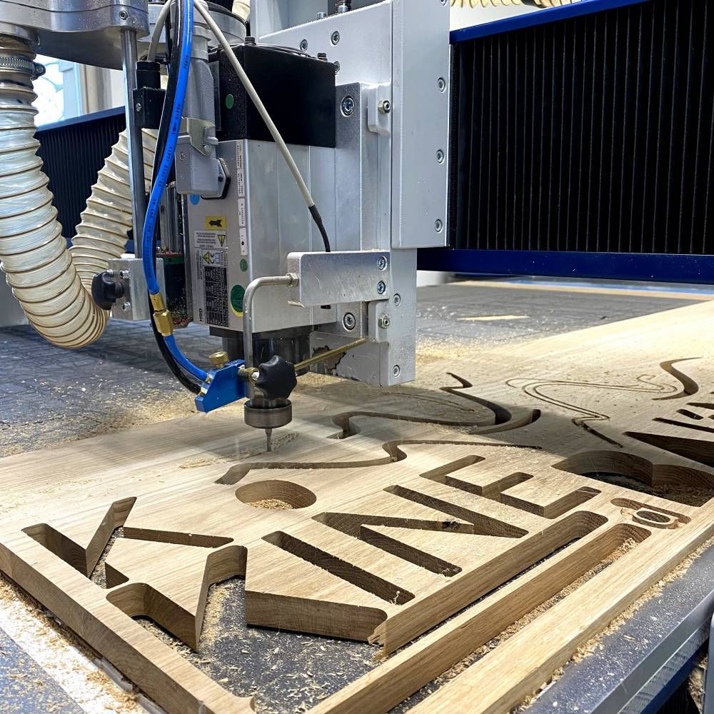 Une fraiseuse CNC découpe des lettres en bois dans une plaque de contreplaqué, dans un atelier