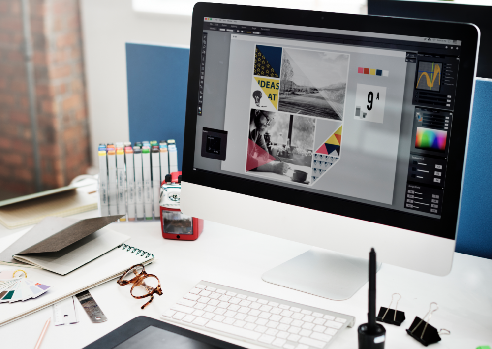 Espace de travail avec un grand écran affichant une mise en page, un clavier et des outils de dessin posés sur un bureau