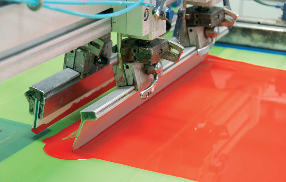 Une machine de sérigraphie applique de l’encre rouge vif sur du tissu dans un atelier