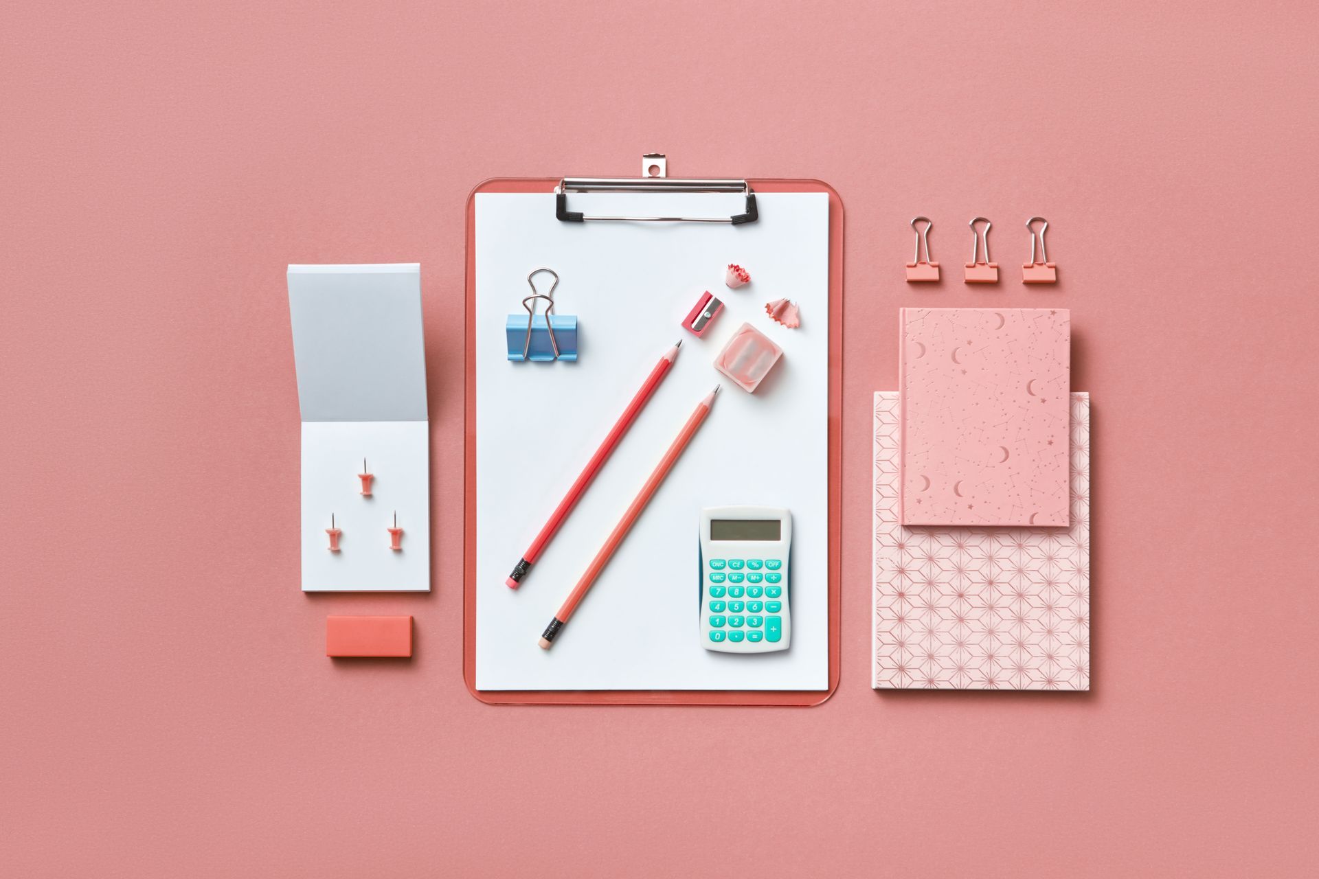 Vue de dessus de fournitures de bureau roses : porte-bloc, stylos, calculatrice et bloc-notes sur fond rose