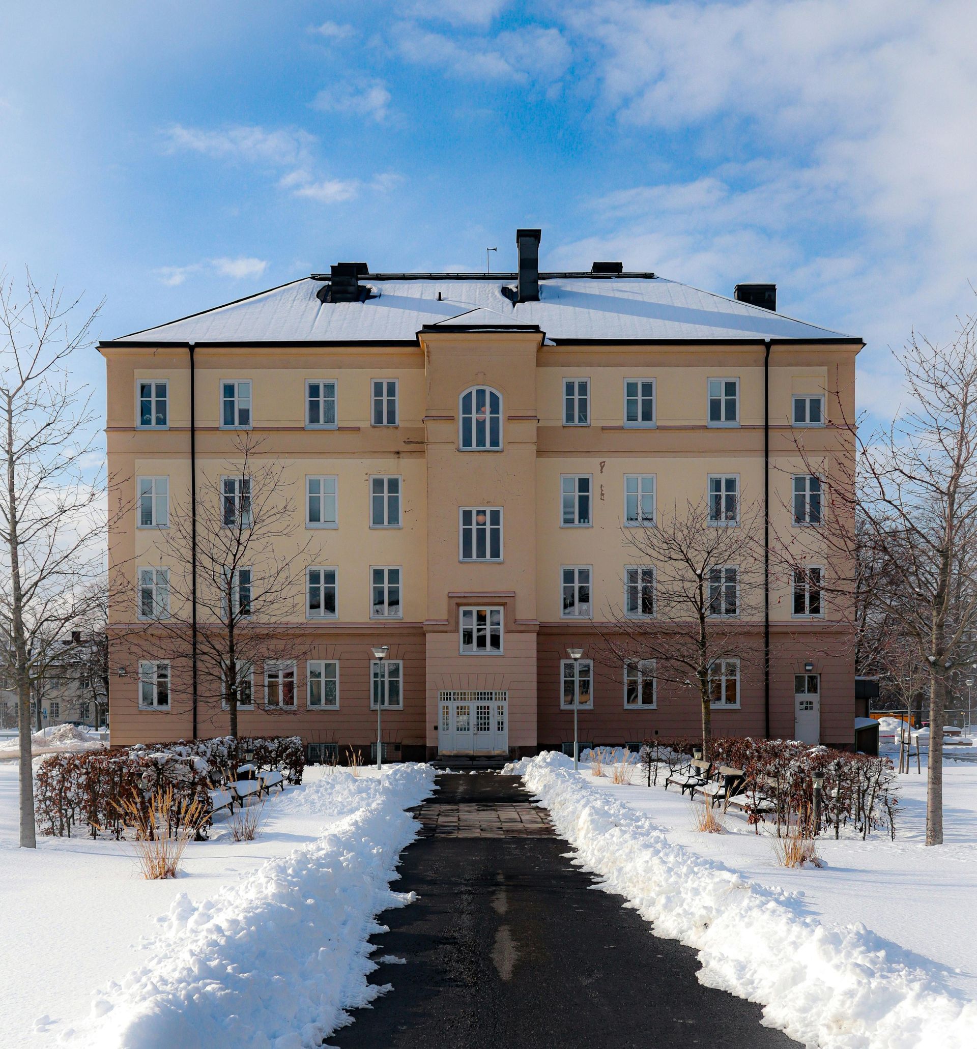 Luminen kävelytie, joka johtaa beigenväriseen kerrostaloon sinisen talvitaivaan alla