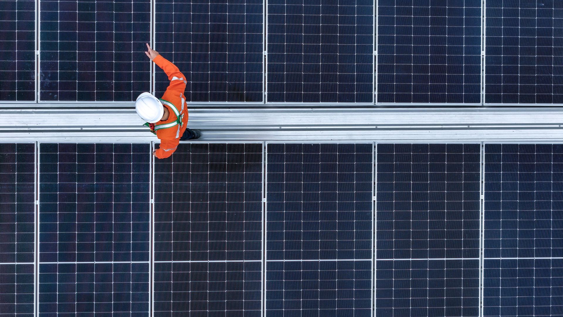 Un ouvrier en tenue de sécurité orange inspecte des panneaux solaires sur un toit.
