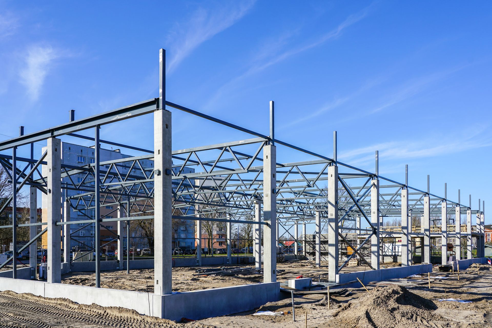 Bâtiment à ossature métallique en construction sur un terrain de gravier sous un ciel bleu azur.