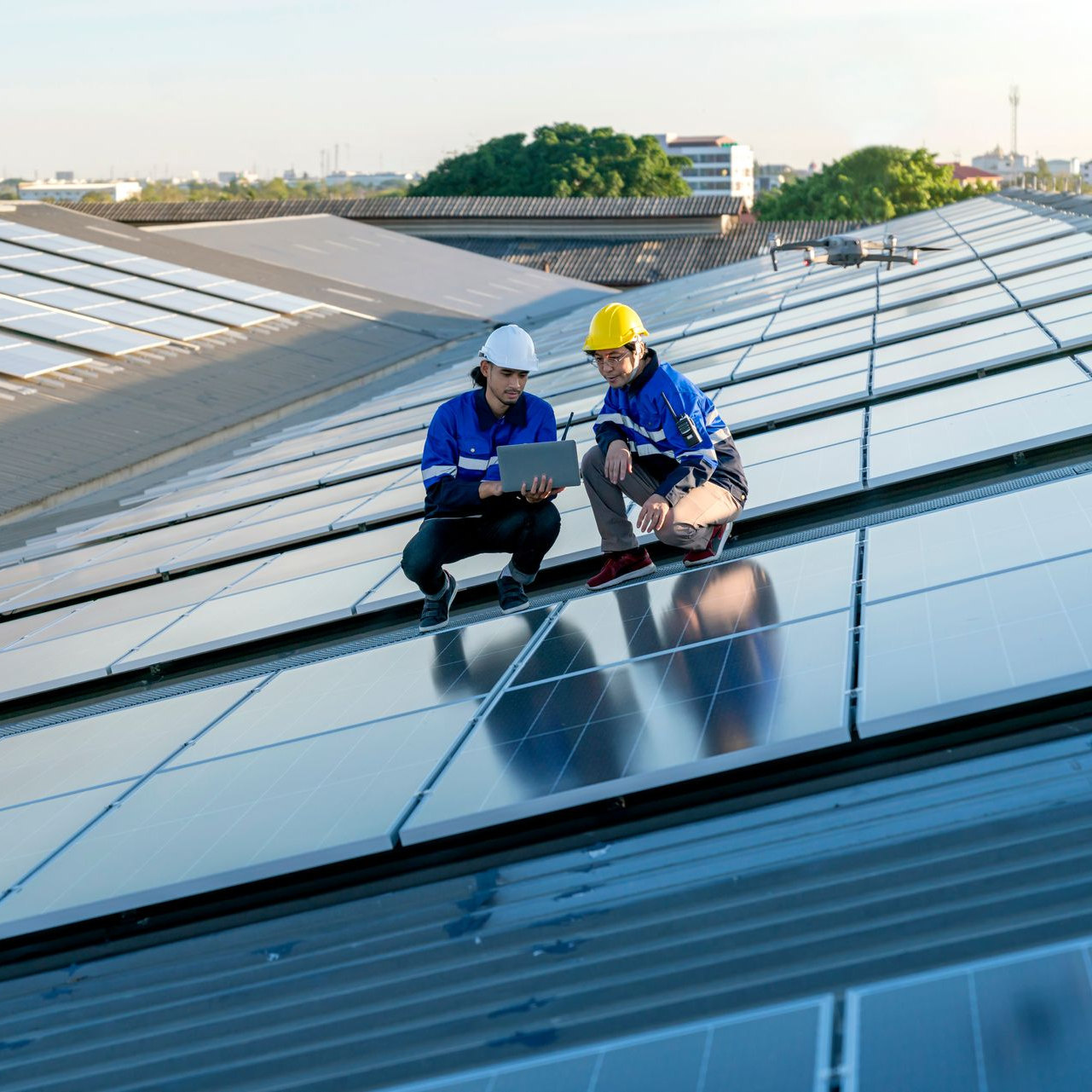 Deux ingénieurs portant des casques de chantier inspectent des panneaux solaires sur un toit en plein jour.