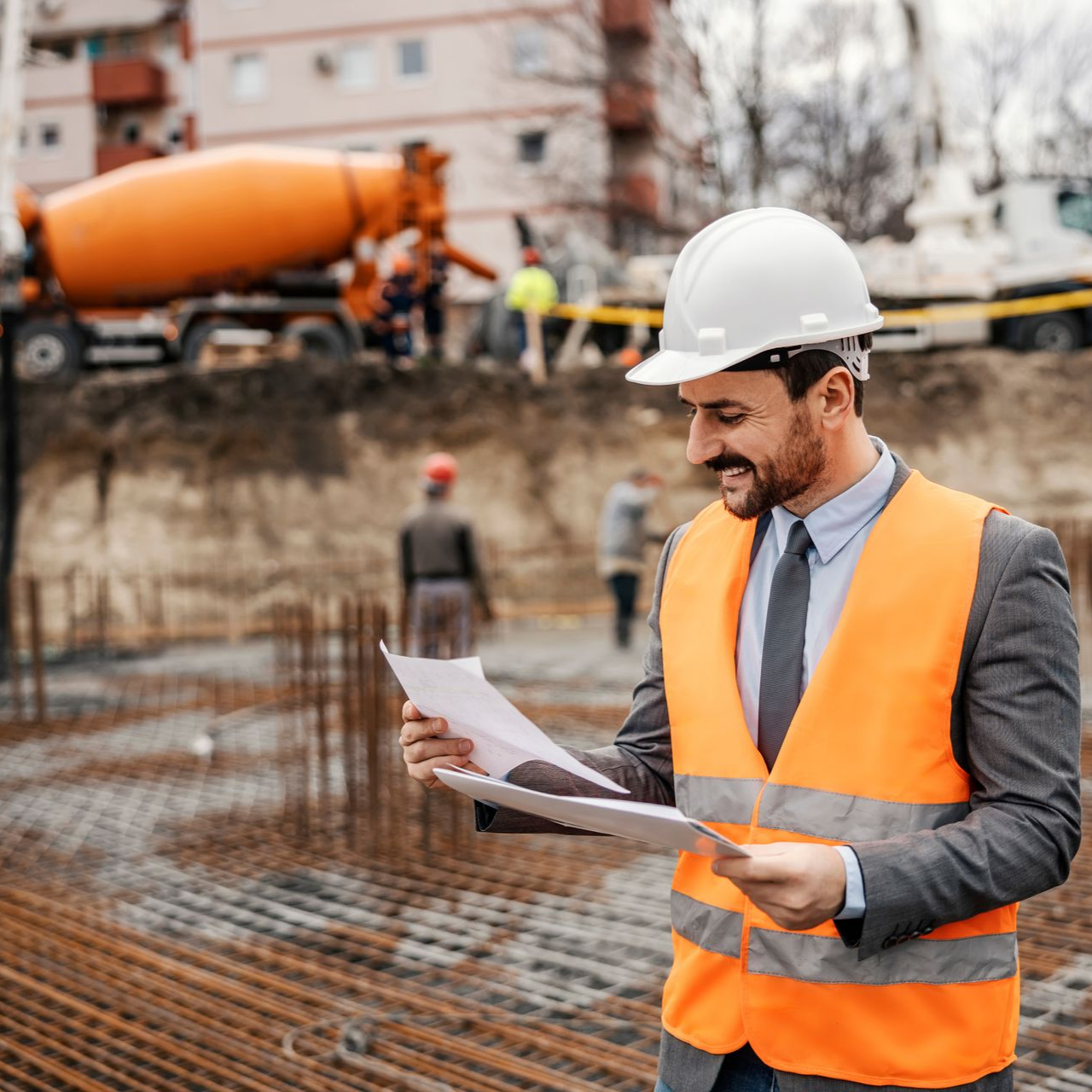Ouvrier du bâtiment portant un gilet de sécurité orange et un casque de chantier examine des plans sur un chantier.