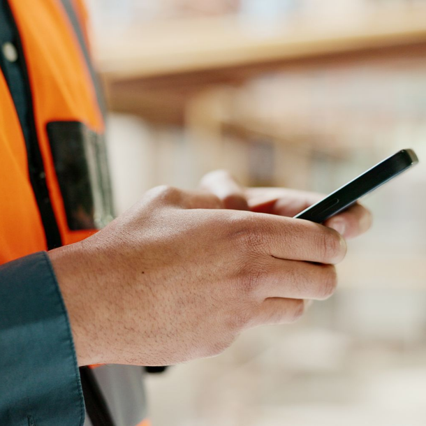 Gros plan sur un travailleur portant un gilet de sécurité orange utilisant un smartphone