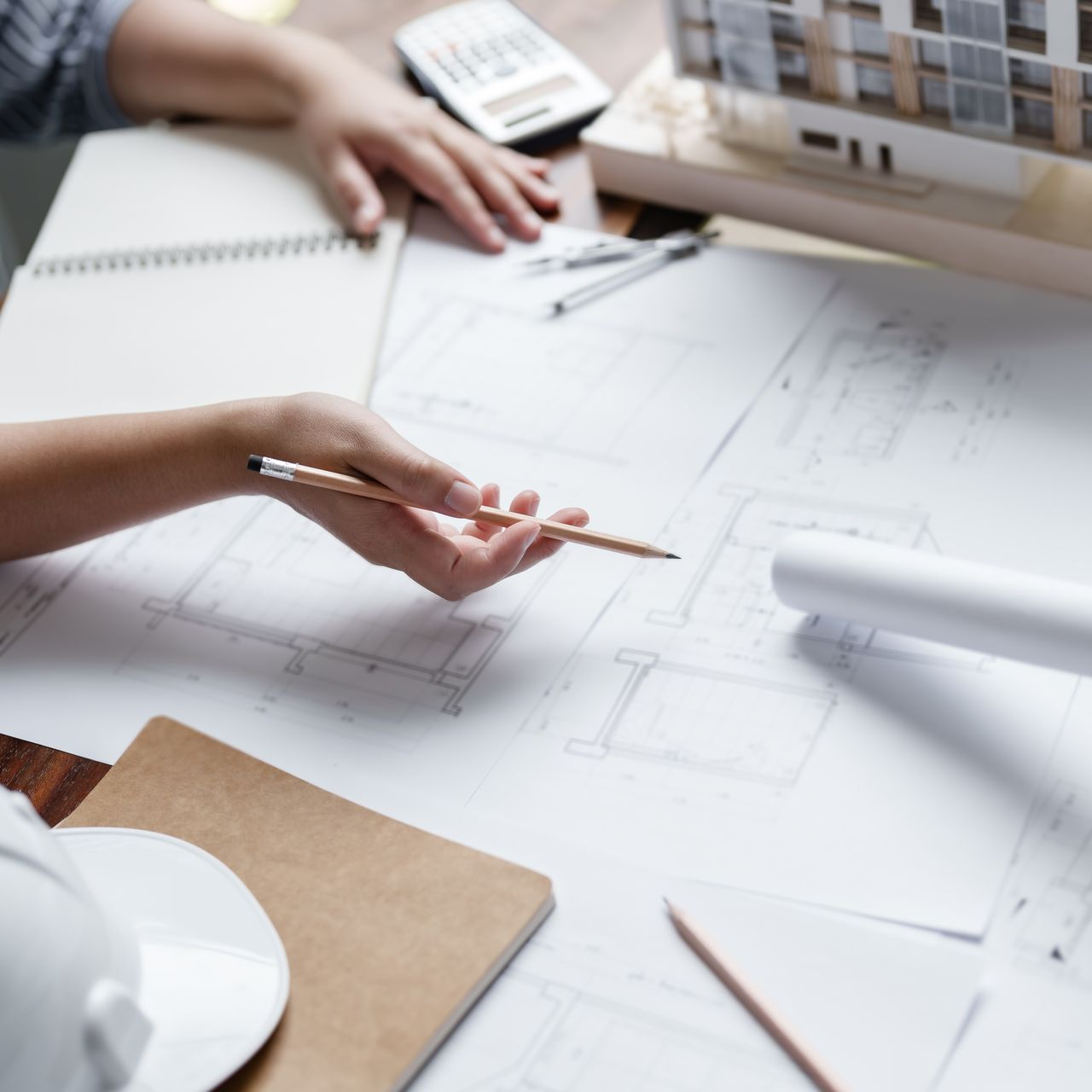 Des mains dessinent des plans architecturaux sur un bureau, à l'aide d'un crayon et d'un carnet.