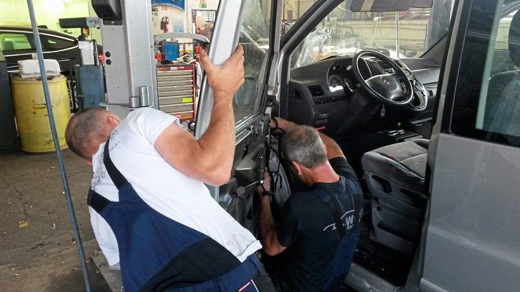 Zwei Männer arbeiten in einer Garage an der Tür eines Autos.