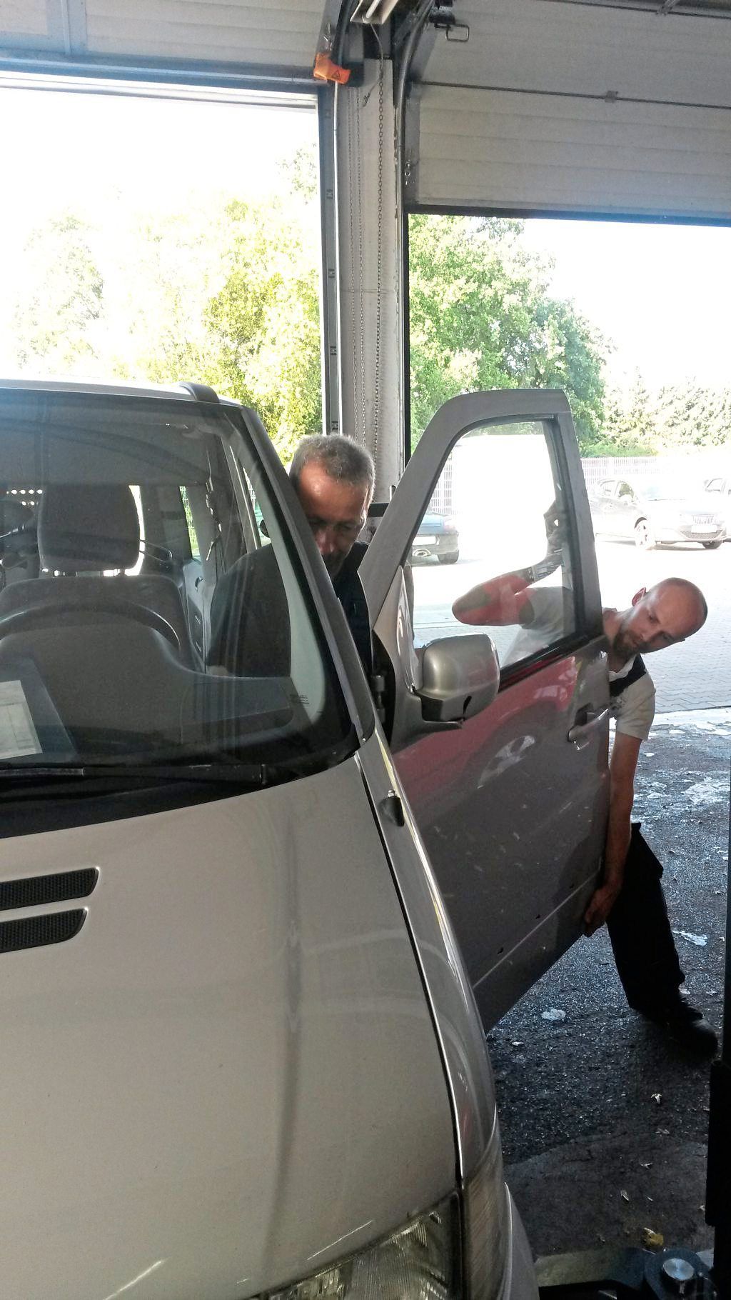 Zwei Männer arbeiten in einer Garage an der Tür eines Autos.