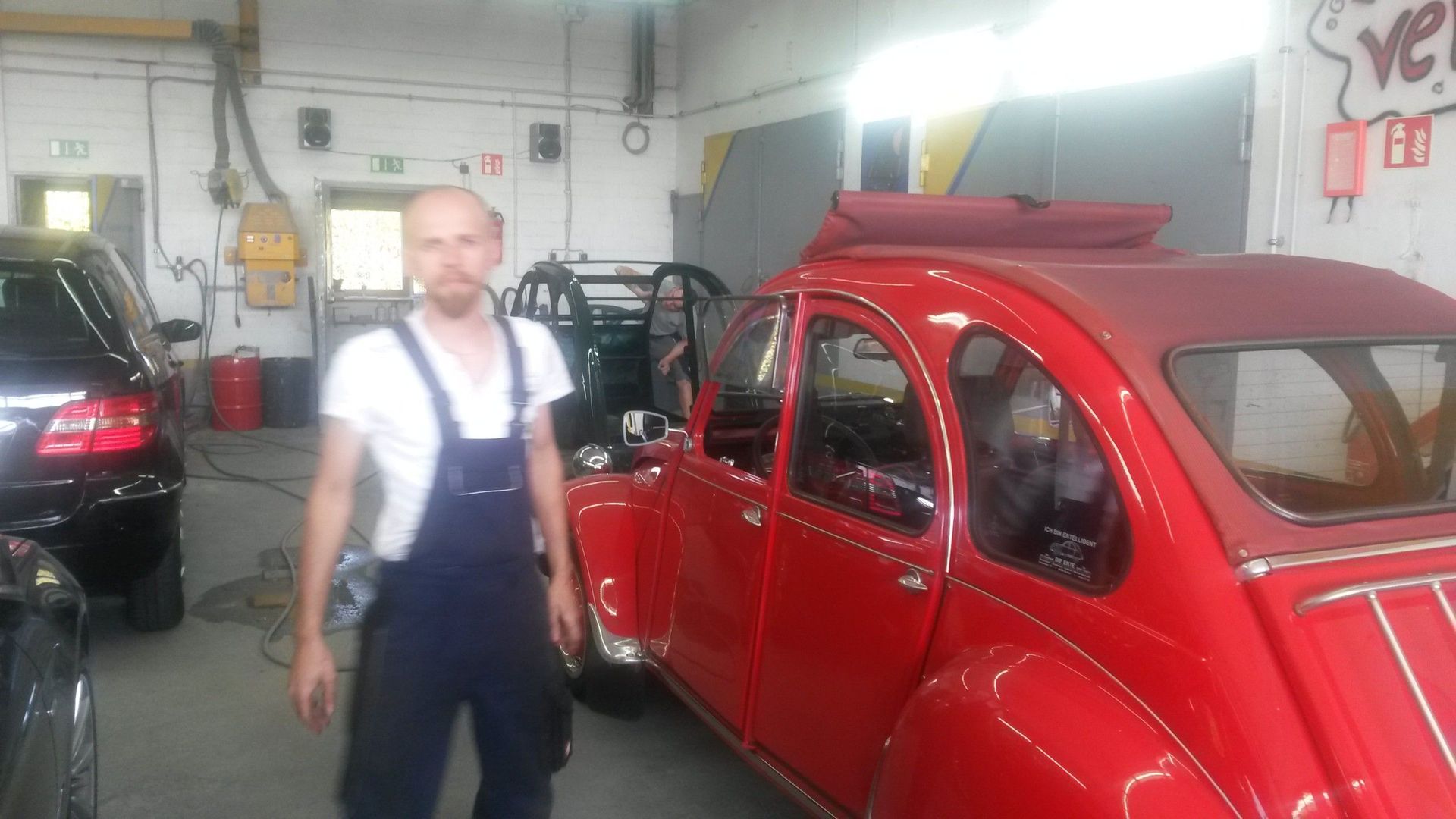 Ein Mann steht vor einem roten Auto in einer Garage.