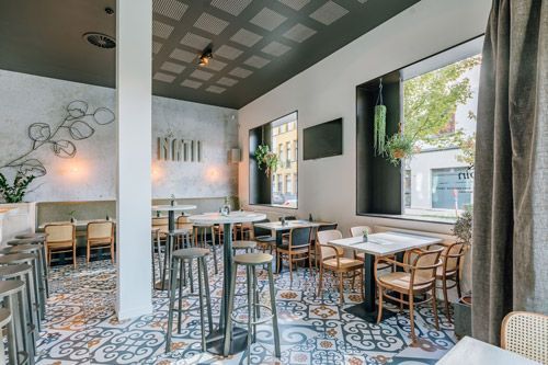 Intérieur du restaurant avec tables, chaises, tabourets de bar, sol à motifs et grandes fenêtres.